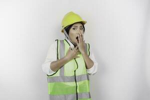 un' ritratto di un' scioccato asiatico donna lavoro duro e faticoso indossare sicurezza casco e veste mentre sua bocca largo aprire, isolato di bianca sfondo. lavoro giorno concetto foto