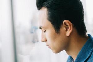 uomo asiatico triste vicino alla finestra foto
