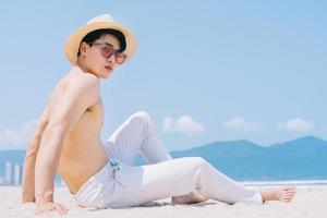 giovane asiatico senza sella seduto sulla sabbia e guardando il mare