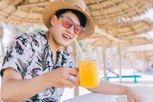 giovane uomo asiatico che beve succo d'arancia sulla spiaggia? foto