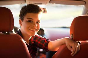 felice e bella donna afroamericana con i capelli corti in macchina, stile di vita foto
