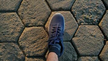 avvicinamento tiro di piedi indossare scarpe da ginnastica su un' mattone strada illuminato di il crescente sole. foto