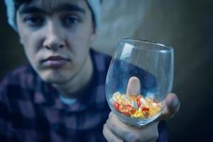 ragazzo triste con in mano un bicchiere di pillole e medicine. foto