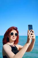 donna dai capelli rossi prende selfie sulla fotocamera dello smartphone. foto