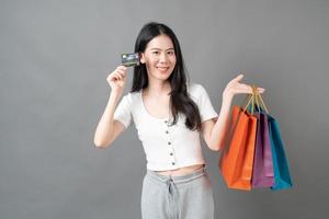 giovane donna asiatica mano azienda shopping bag e carta di credito su sfondo grigio foto