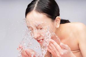 bella donna asiatica si lava il viso con acqua pura foto