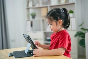 asiatico bambino ragazza guardare utilizzando e toccare tavoletta Schermo schermo. bambino sorridente divertente tempo per uso tavoletta. pure tanto schermo volta. carino ragazza Guardando video mentre tv, Internet dipendenza concetto. foto