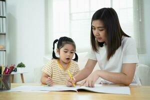 carino poco bambino pittura con colorato vernici. asiatico ragazza e madre utilizzando pastello disegno colore. figlia e mamma fare compiti a casa colorazione cartone animato personaggi. bambino artista attività stile di vita concetto. foto