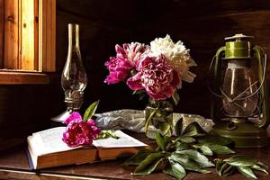 natura morta di oggetti vintage e un bouquet di peonie su un tavolo vicino alla finestra in una vecchia casa di paese. foto