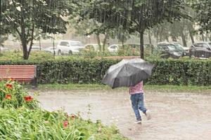 una bambina si diverte a correre con un ombrello sotto la pioggia battente. giorno di pioggia foto