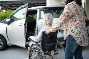 aiutare e supportare la donna anziana o anziana asiatica paziente seduta su sedia a rotelle prepararsi a raggiungere la sua auto, concetto medico sano e forte foto