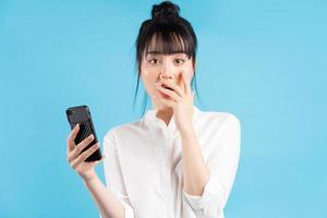 bella donna asiatica che tiene il telefono su sfondo blu con espressione sorpresa