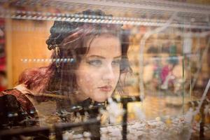 giovane, una splendida donna dai capelli rossi vestita con abiti di moda retrò, guarda attraverso la vetrina di una gioielleria. foto