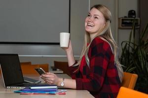 donna bionda sorridente che si siede a un computer portatile che beve tè e lavora. foto