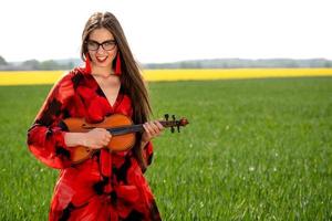 giovane donna in abito rosso suona il violino in un prato verde - immagine foto