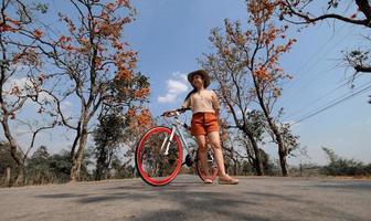 donna in piedi accanto alla sua bici all'aperto a palash tree con uno sfondo di bellissimi fiori d'arancio foto