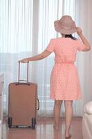 donna turistica asiatica in un vestito rosa in piedi con i suoi bagagli nella camera da letto dell'hotel foto