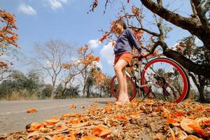 donna in piedi accanto alla sua bici all'aperto a palash tree con uno sfondo di bellissimi fiori d'arancio foto