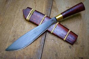 coltello personalizzato o enep nel fodero in legno naturale sul vecchio sfondo del tavolo fatto a mano in thailandia foto