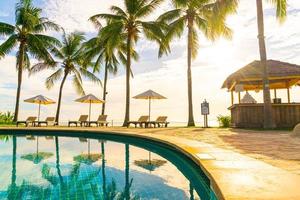 bellissimi ombrelloni e sedie di lusso intorno a una piscina all'aperto in hotel e resort con palme da cocco sul cielo al tramonto o all'alba - concetto di vacanza e vacanza foto