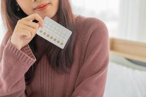 donna asiatica che tiene la pillola anticoncezionale foto