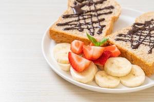 pane integrale tostato con banana fresca, fragola e cioccolato per colazione foto