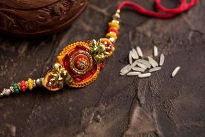 sfondo raksha bandhan con un elegante rakhi e riso sparso. un tradizionale cinturino da polso indiano che è un simbolo di amore tra fratelli e sorelle. foto