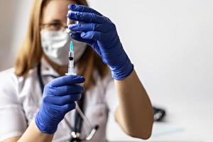 una dottoressa che indossa una maschera medica aspira il vaccino contro il coronavirus in una siringa presso la clinica. il concetto di vaccinazione, immunizzazione, prevenzione contro covid-19.