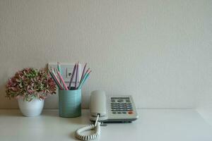 telefono e matite pastello nel vetro blu sulla scrivania sullo sfondo del muro grigio foto