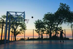 nero uomo fare gli sport, giocando pallacanestro su Alba, silhouette foto