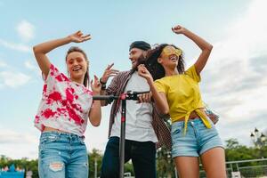 contento giovane azienda di sorridente amici danza a piedi nel strada con elettrico calcio scooter foto