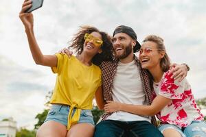 contento giovane azienda di sorridente amici seduta nel parco foto