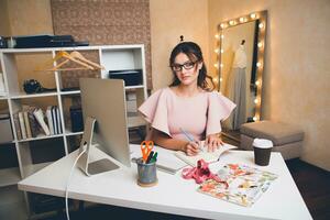 donna nel rosa lusso vestire, estate tendenza, moda progettista Lavorando a ufficio su computer foto