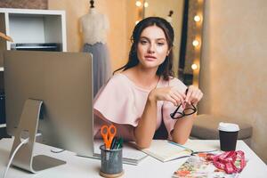 donna nel rosa lusso vestire, estate tendenza, moda progettista Lavorando a ufficio su computer foto