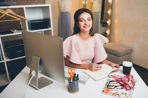 donna nel rosa lusso vestire, estate tendenza, moda progettista Lavorando a ufficio su computer foto