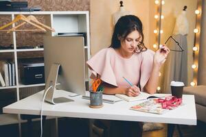 donna nel rosa lusso vestire, estate tendenza, moda progettista Lavorando a ufficio su computer foto