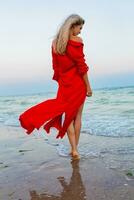 bellissimo gratuito donna nel rosso vestito nel vento su mare spiaggia foto