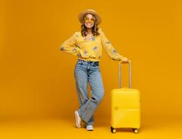 sorridente donna in viaggio con valigia vestito nel di moda attrezzatura su luminosa giallo sfondo, positivo estate vacanza foto