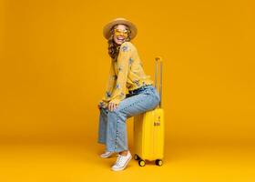 sorridente donna in viaggio con valigia vestito nel di moda attrezzatura su luminosa giallo sfondo, positivo estate vacanza foto