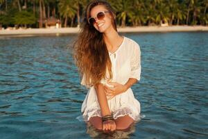 sottile bellissimo donna nel bianca cotone vestito a piedi su tropicale spiaggia foto