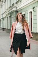 giovane elegante bellissimo donna a piedi nel strada, indossare rosa cappotto foto