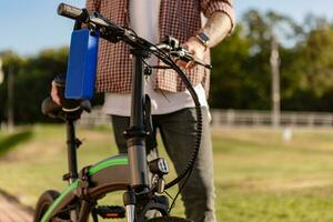 dettagli di fricchettone elegante uomo nel parco ascoltando per musica su utilizzando elettrico bicicletta foto