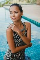 giovane asiatico sexy bellissimo donna nel tropicale vestire, zebra Stampa, in posa nel piscina foto