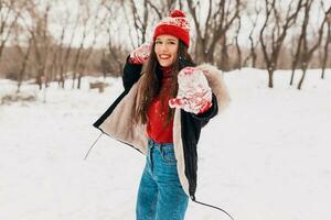 giovane bella sorridente contento donna nel rosso guanti e a maglia cappello indossare inverno cappotto, a piedi nel parco nel neve, caldo Abiti foto