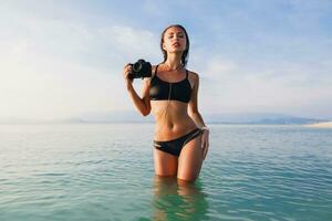 bellissimo donna, abbronzato pelle, nero bikini costume da bagno, in piedi nel blu acqua foto