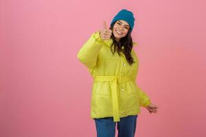 attraente attivo donna in posa su rosa sfondo nel colorato inverno giù giacca di luminosa giallo colore, sorridente divertimento, caldo cappotto moda tendenza, pazzo scioccato sorpreso viso espressione foto