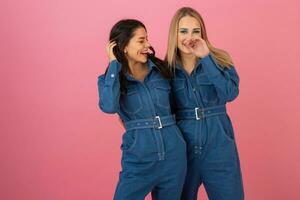 Due eccitato attraente ragazza amici attivo donne in posa su rosa sfondo nel denim complessivamente avendo divertimento insieme moda tendenza foto