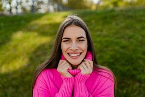 giovane sorridente donna nel rosa maglione a piedi nel verde parco foto