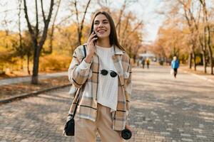 attraente giovane donna a piedi nel autunno indossare giacca utilizzando Telefono foto