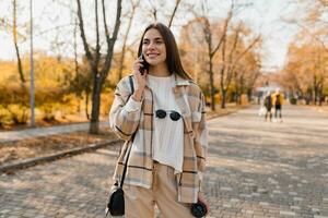 attraente giovane donna a piedi nel autunno indossare giacca utilizzando Telefono foto